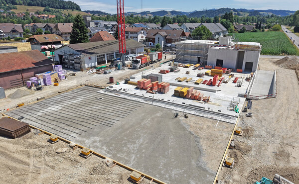 Drohnenaufnahme der Baustelle mit frisch betonierter Bodenplatte, Schalungselementen und Baumaterialien.