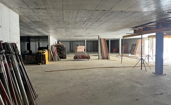 Grosszügiger Innenraum im Betonrohbau mit gelagerten Schalungselementen und Baustützen.