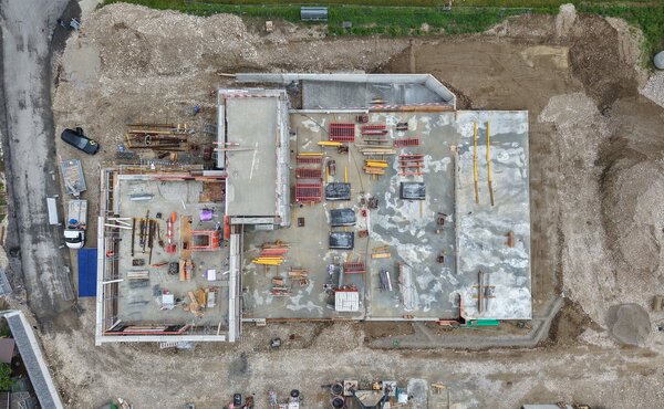 Senkrechte Drohnenaufnahme des Neubaus mit Bodenplatten, Betonwänden, Schalungen und Baumaterialien.