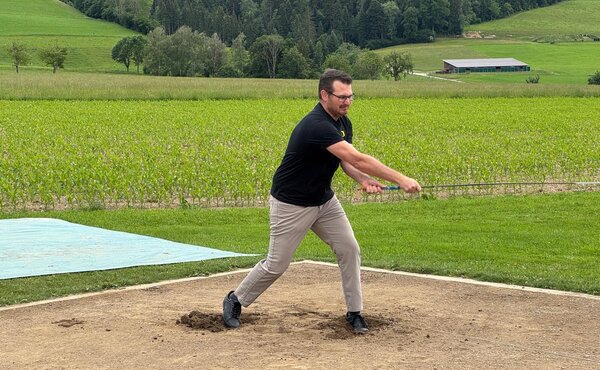 Teilnehmer beim Hornusserabschlag mit grünen Hügeln im Hintergrund.