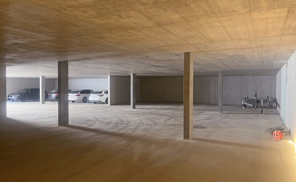 Innenansicht der neuen Tiefgarage mit Betonstützen, parkierten Fahrzeugen und einem Anhänger.