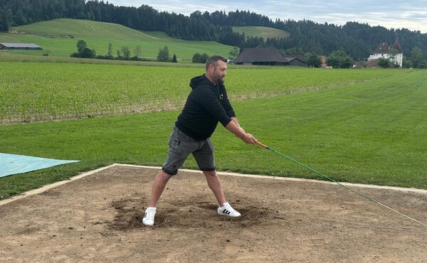 Teilnehmer beim Hornussen auf dem Abschlagplatz mit Blick über die Emmentaler Landschaft.