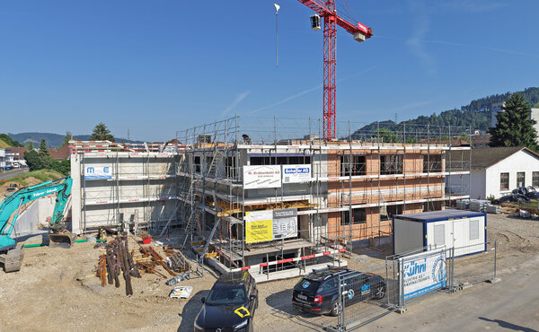 Rohbau des neuen Bürogebäudes und der Lagerhalle in Lützelflüh mit Baugerüst und rotem Baukran.