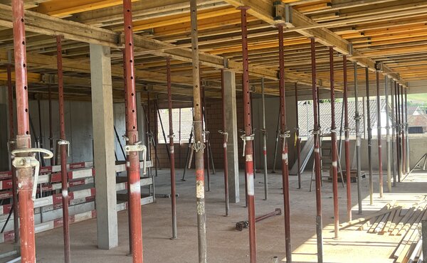 Innenraum des Rohbaus mit dichter Deckenschalung aus Holz und zahlreichen roten Baustützen.