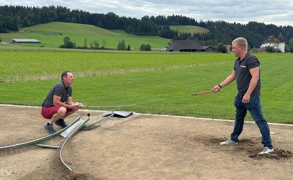 Zwei Männer bereiten gemeinsam den Hornusserabschlag vor.